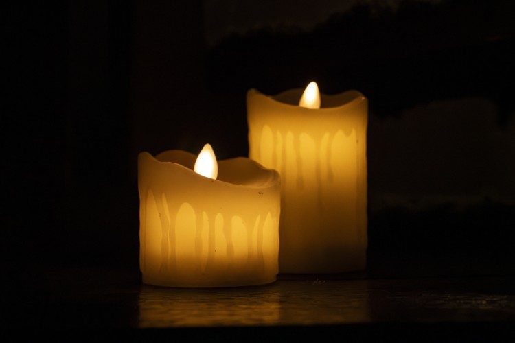 Twee brandende kaarsen met een warme gloed op een donkere achtergrond. De kaarsen hebben een natuurlijke, gesmolten uitstraling aan de bovenkant.